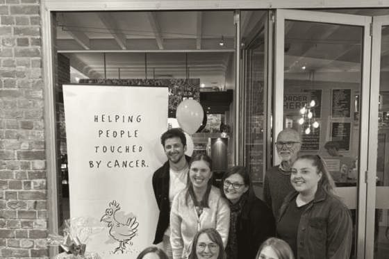 Supporters at the 2025 Quiz Night holding a raffle hamper in front of a 'Helping people touched by cancer' banner